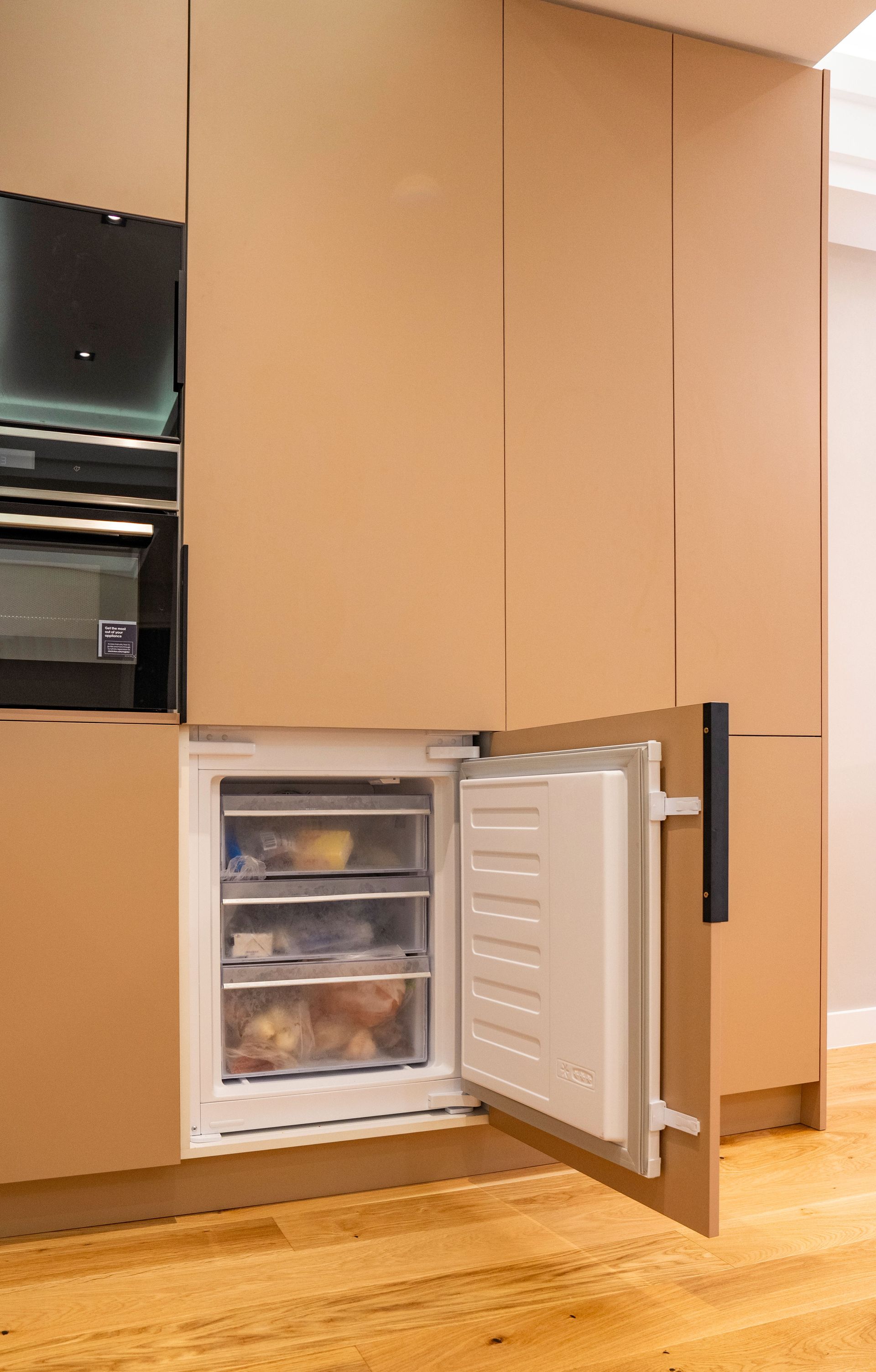 Open integrated freezer in a modern kitchen setup, showcasing storage solution.